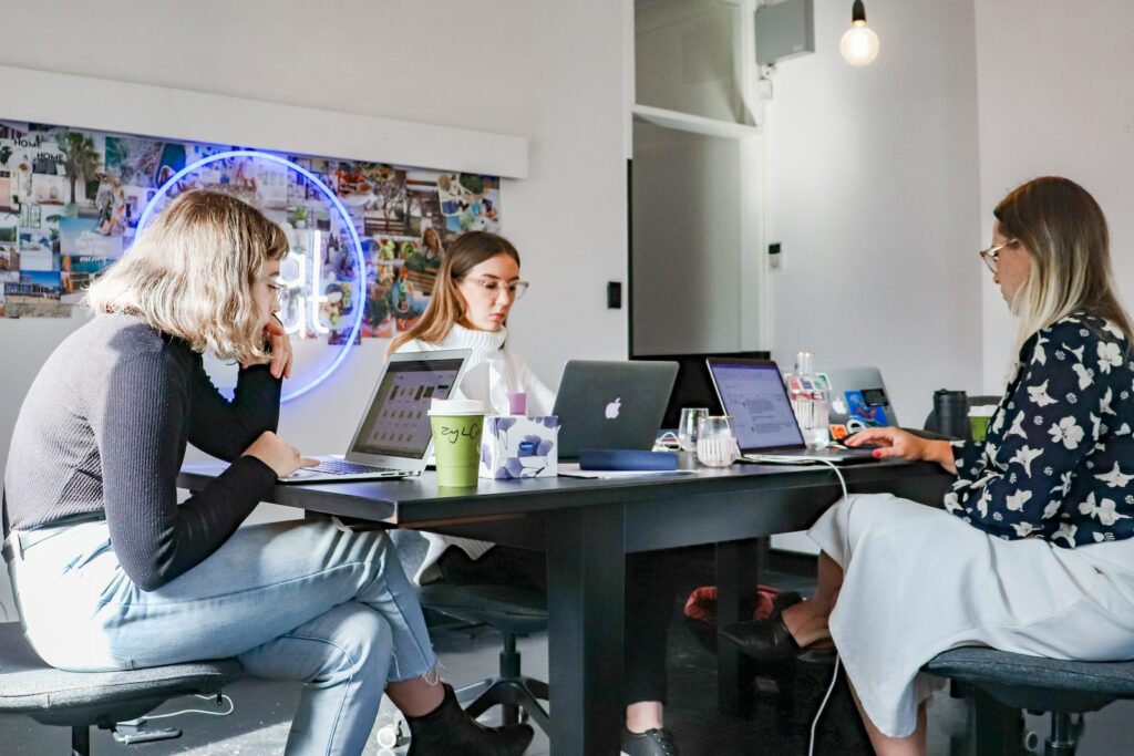 3 women sitting on chair in front of table with laptop computers